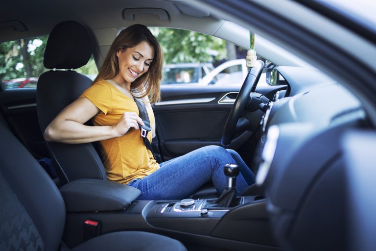 Beautiful female driver putting seat belt on before driving a car.